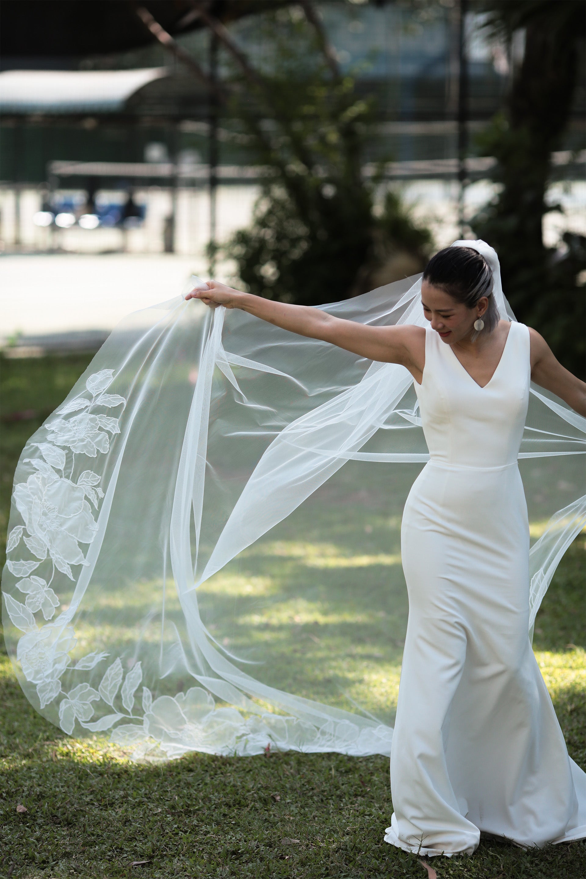 A bride in a white dress holding a cathedral organza floral veil that is flowing in the wind.